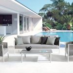 Thumbnail of http://Terrasse%20extérieure%20moderne%20avec%20mobilier%20blanc,%20dont%20deux%20chaises,%20un%20canapé%20trois%20places%20et%20une%20table%20dressée%20à%20côté%20d'une%20piscine%20turquoise.%20Une%20maison%20blanche%20contemporaine%20avec%20de%20grandes%20portes%20vitrées%20s'ouvre%20sur%20la%20terrasse,%20entourée%20de%20verdure%20luxuriante%20et%20de%20grands%20palmiers.