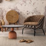 Thumbnail of http://Une%20pièce%20confortable%20avec%20une%20chaise%20en%20rotin%20tressé,%20une%20table%20ronde%20en%20bois%20artistique%20avec%20une%20base%20en%20argile%20unique%20et%20divers%20paniers%20tressés%20et%20objets%20décoratifs.%20Les%20murs%20ont%20une%20texture%20rustique%20et%20patinée%20et%20le%20sol%20est%20recouvert%20d'un%20tapis%20gris%20clair.%20Une%20paire%20de%20sandales%20est%20posée%20sur%20le%20sol.