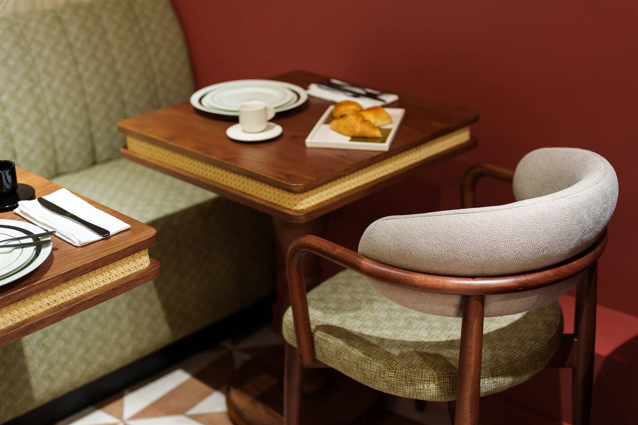 Table en bois cannage et banquette vert olive dans un café rétro. Croissants, vaisselle et café sur la table près d'un mur terre cuite.