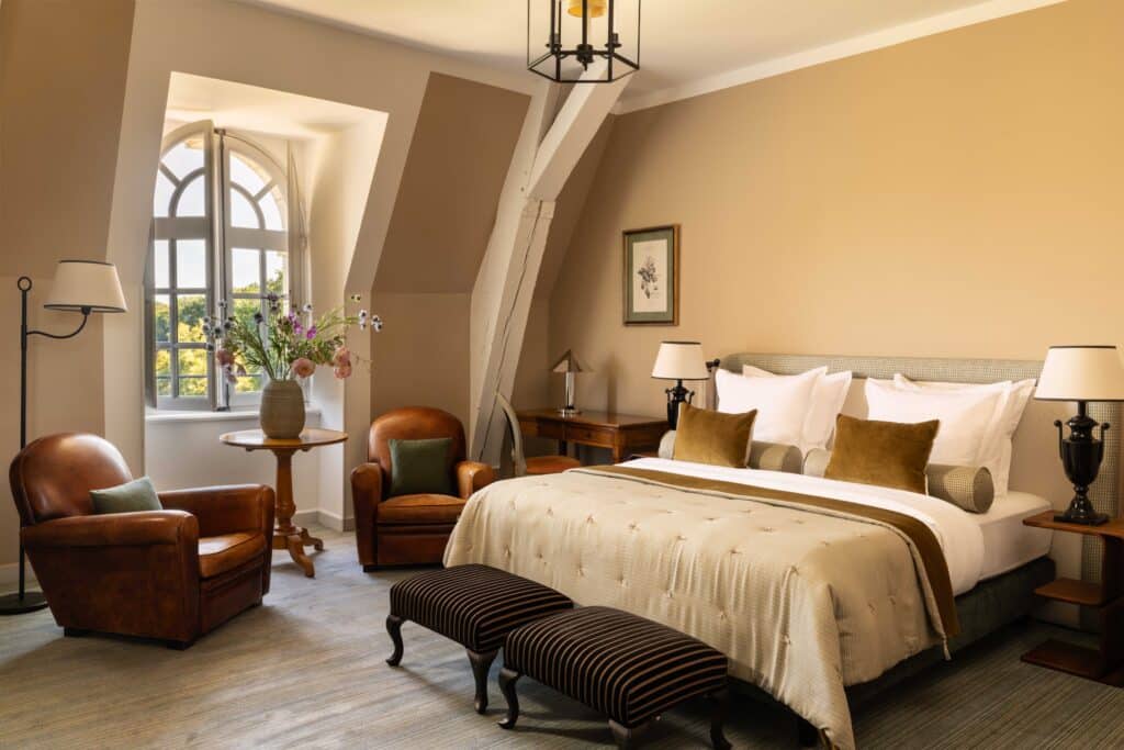 Chambre de Luxe Raffinée avec Mobilier en Cuir Élégant Chambre de luxe raffinée avec grand lit, fauteuils en cuir club et fenêtre cintrée offrant une vue dégagée.
