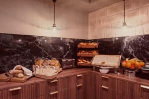Petit-déjeuner buffet avec pains variés, miel en rayon, fruits frais et grille-pain sur plan de travail en bois.