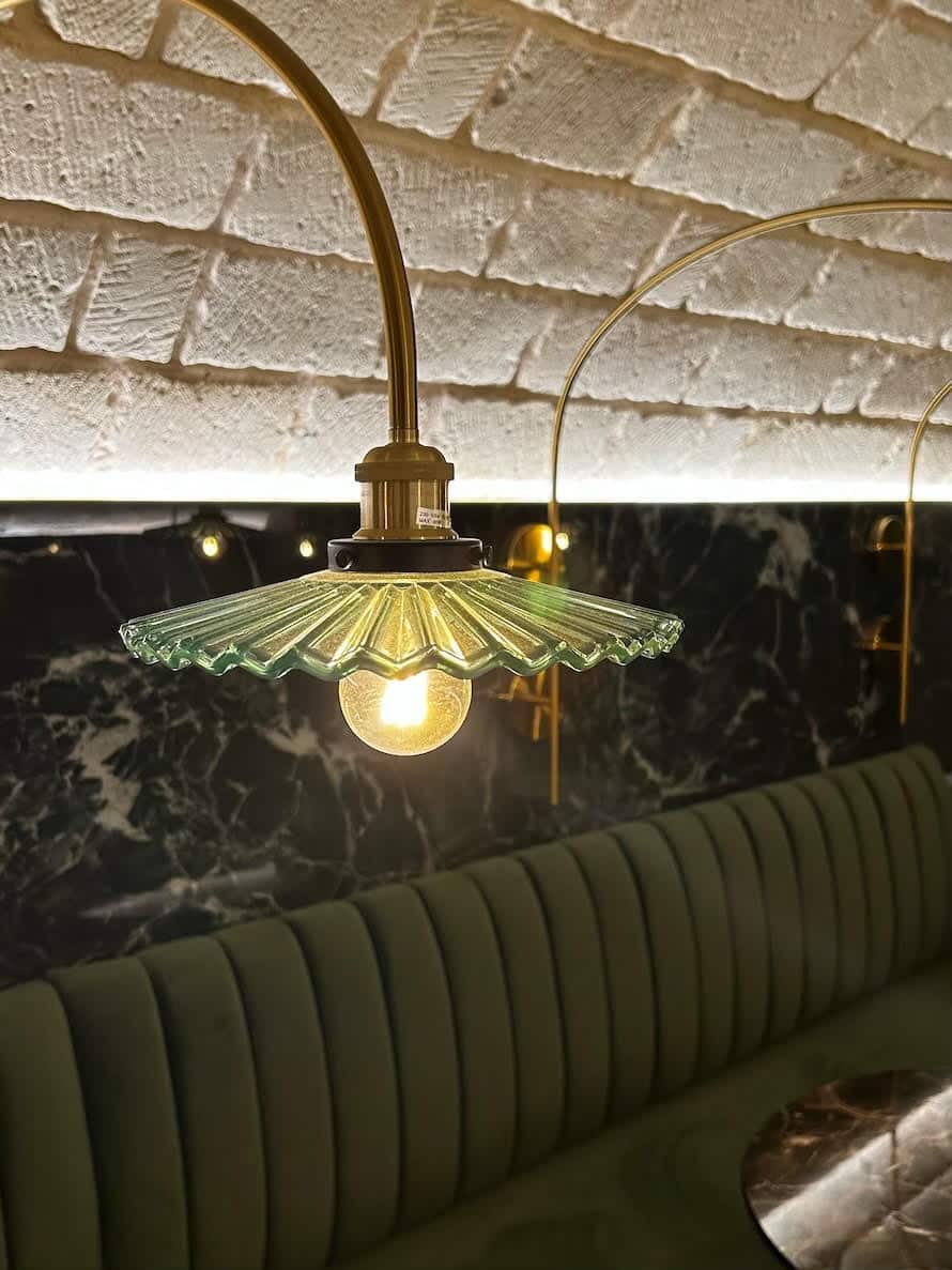 Suspension en verre plissé vert avec bras doré devant un mur en marbre noir et une banquette en velours vert.