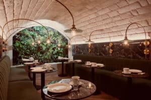 Restaurant chic, plafond voûté, banquettes vertes, tables marbre et mur végétal.