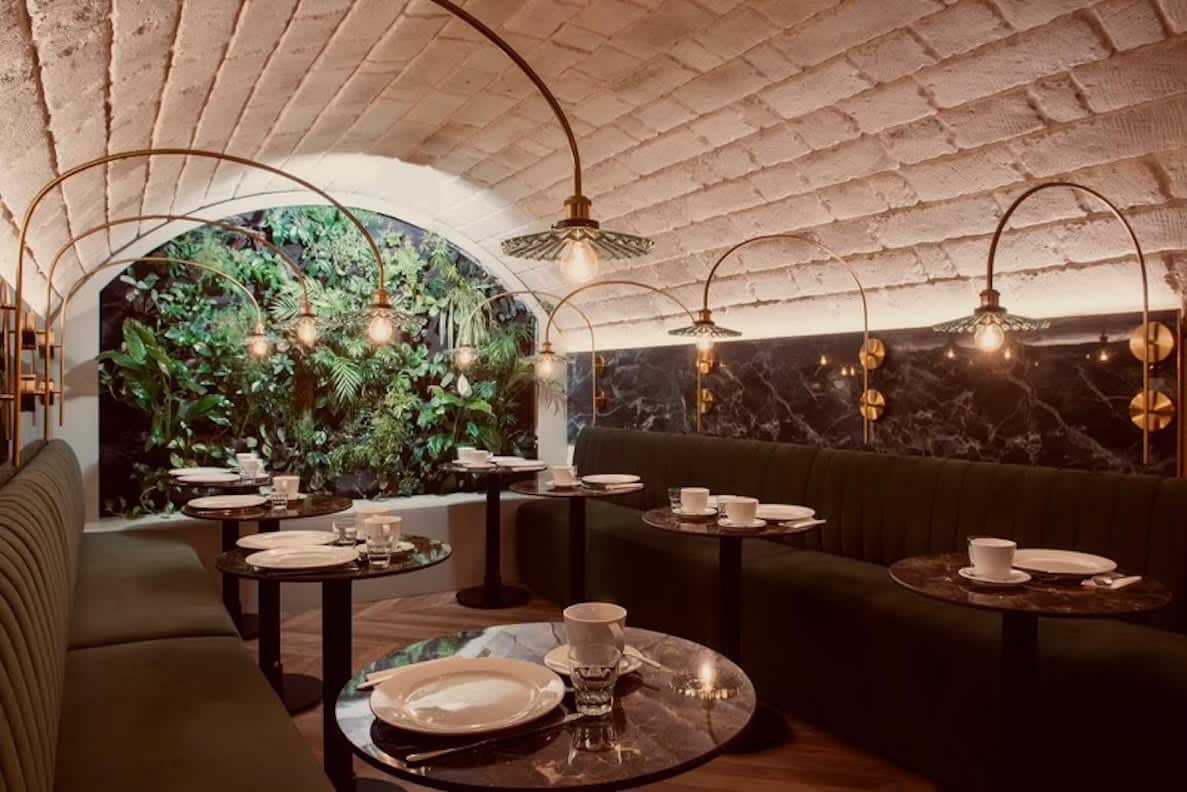 Restaurant chic, plafond voûté, banquettes vertes, tables marbre et mur végétal.